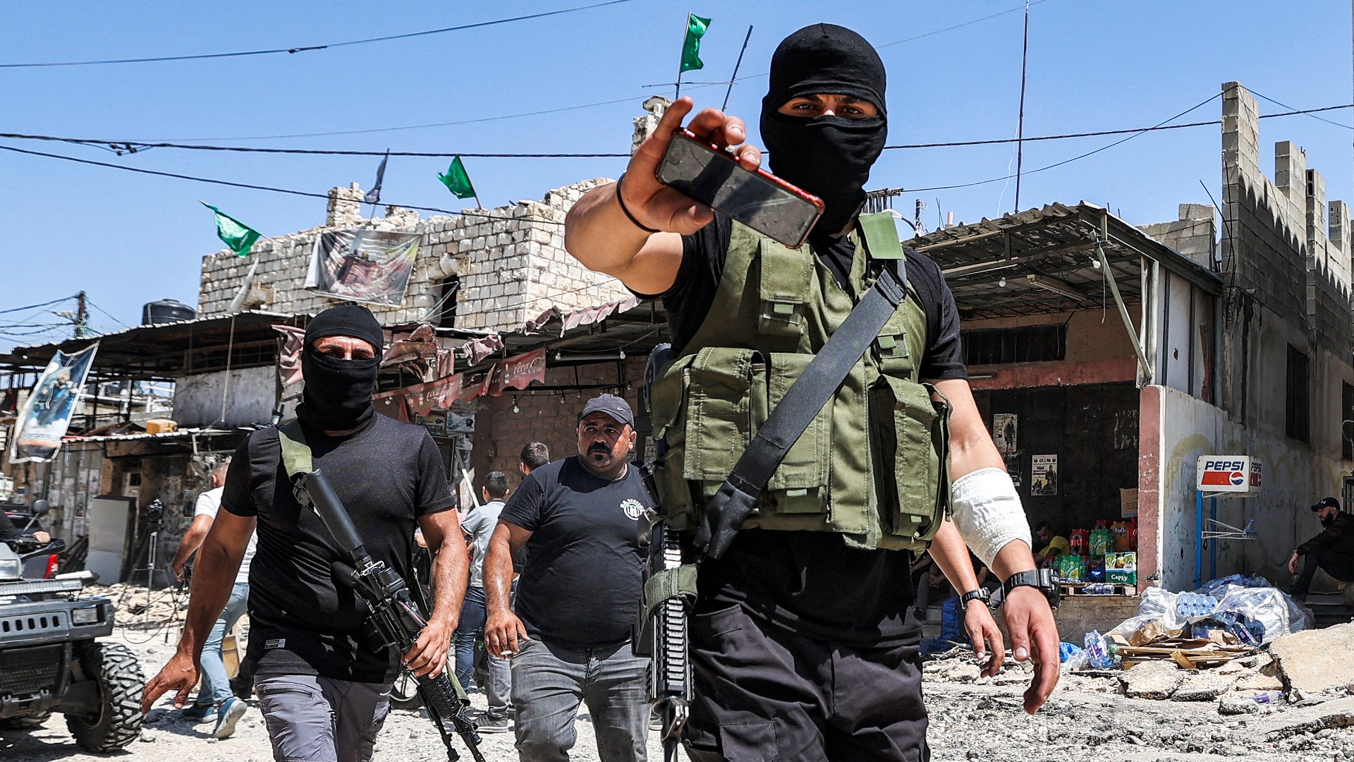 A masked Palestinian fighter gestures with his phone as he walks with others along a street in Jenin in the occupied West Bank on 5 July (AFP)