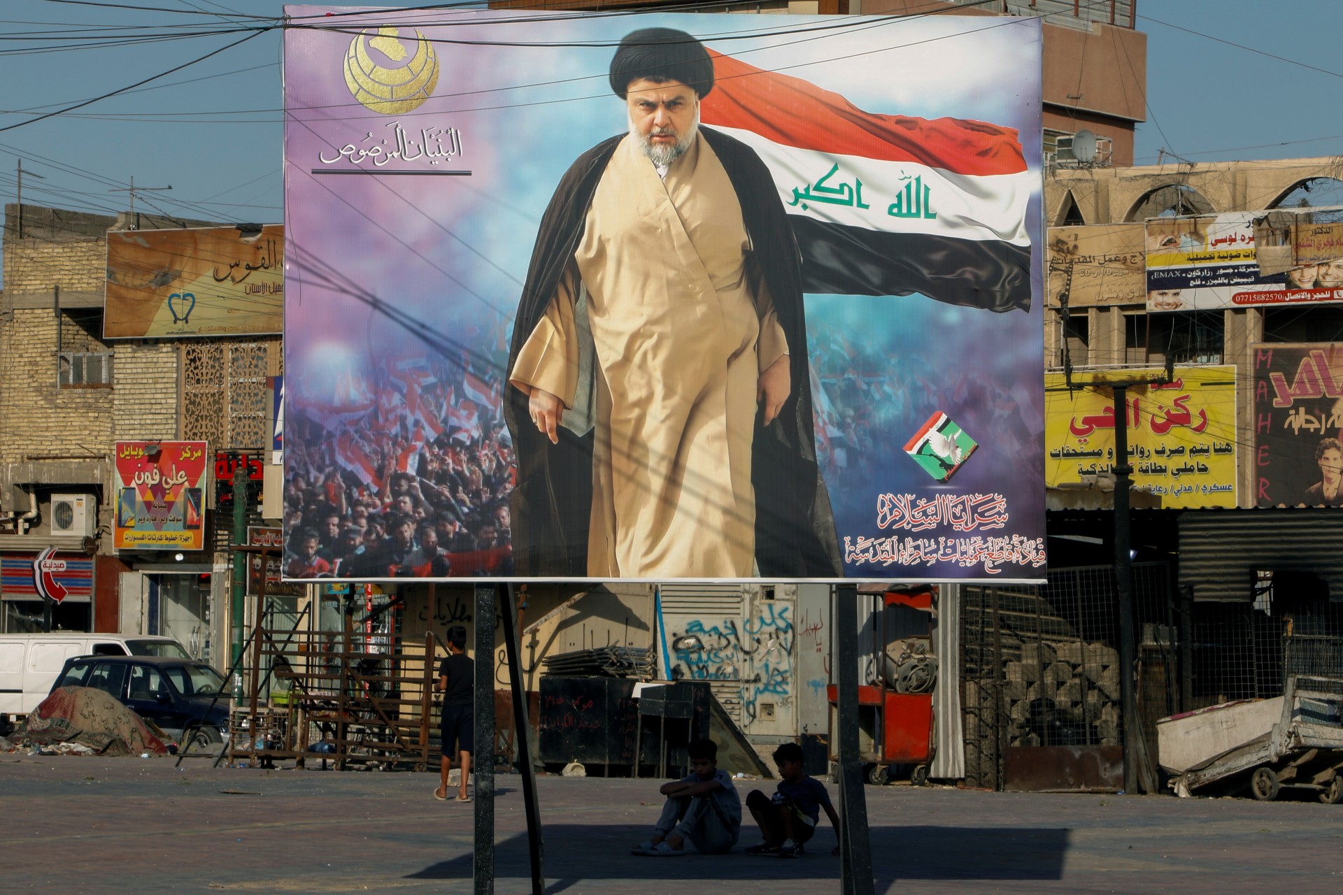 Iraqi boys sit under a poster of Moqtada al-Sadr in the Sadr City district of Baghdad (Reuters)