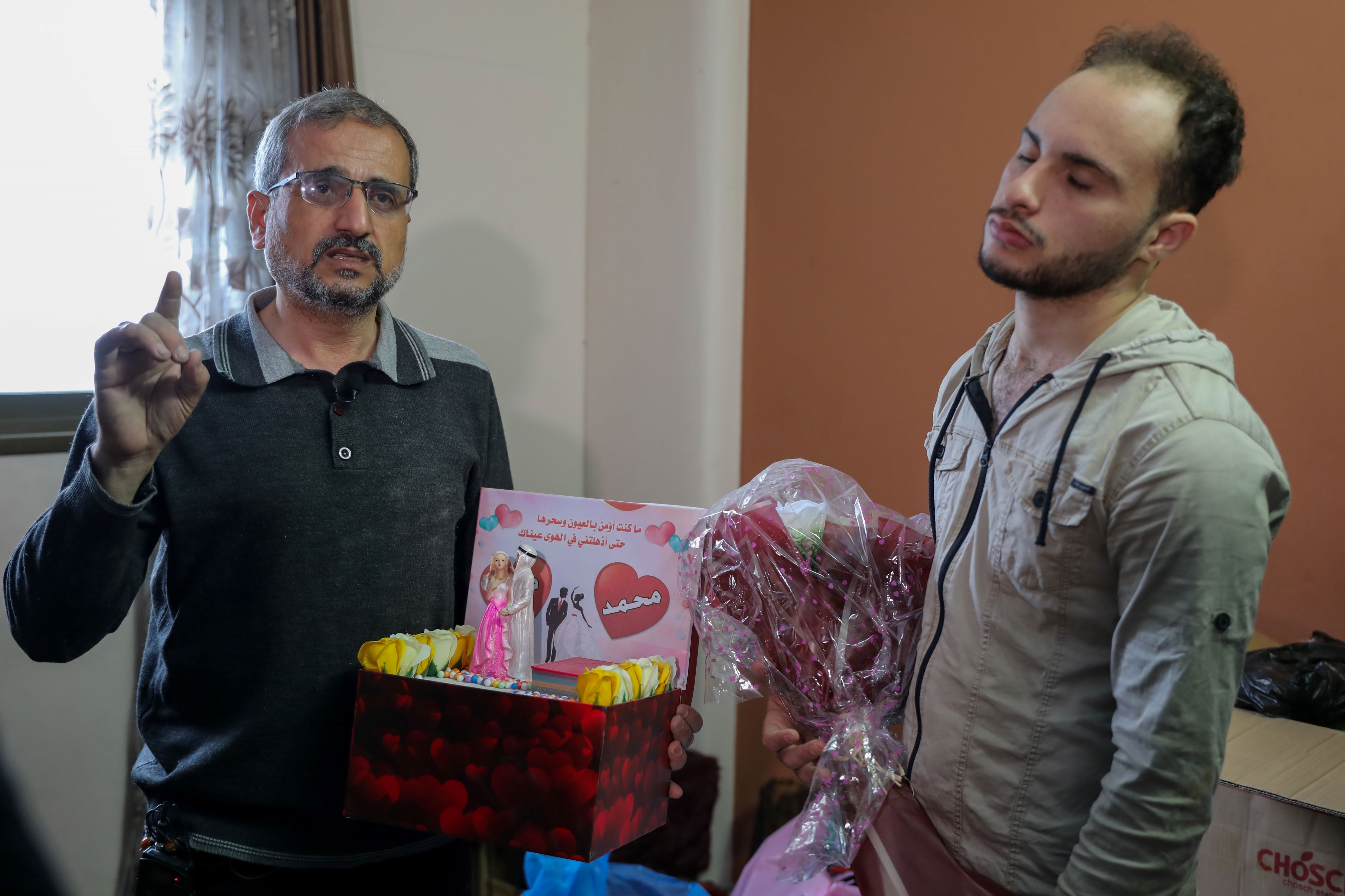 Dania's fiance, Muhammed Saad, holding a flower bouquet he had brought to Dania, and standing next to her father, Alaa, who holds her dowry box (MEE/Muhammed Hajjar)