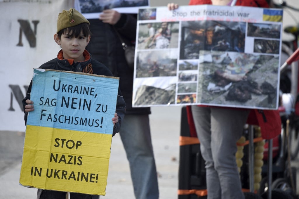Supporters of Ukrainian Pro-Russian rebels hold photos showing damages next to a child holding a poster with the Ukrainian colours reading 'Stop nazis in Ukraine!', Berlin, 16 March 2015 (AFP)