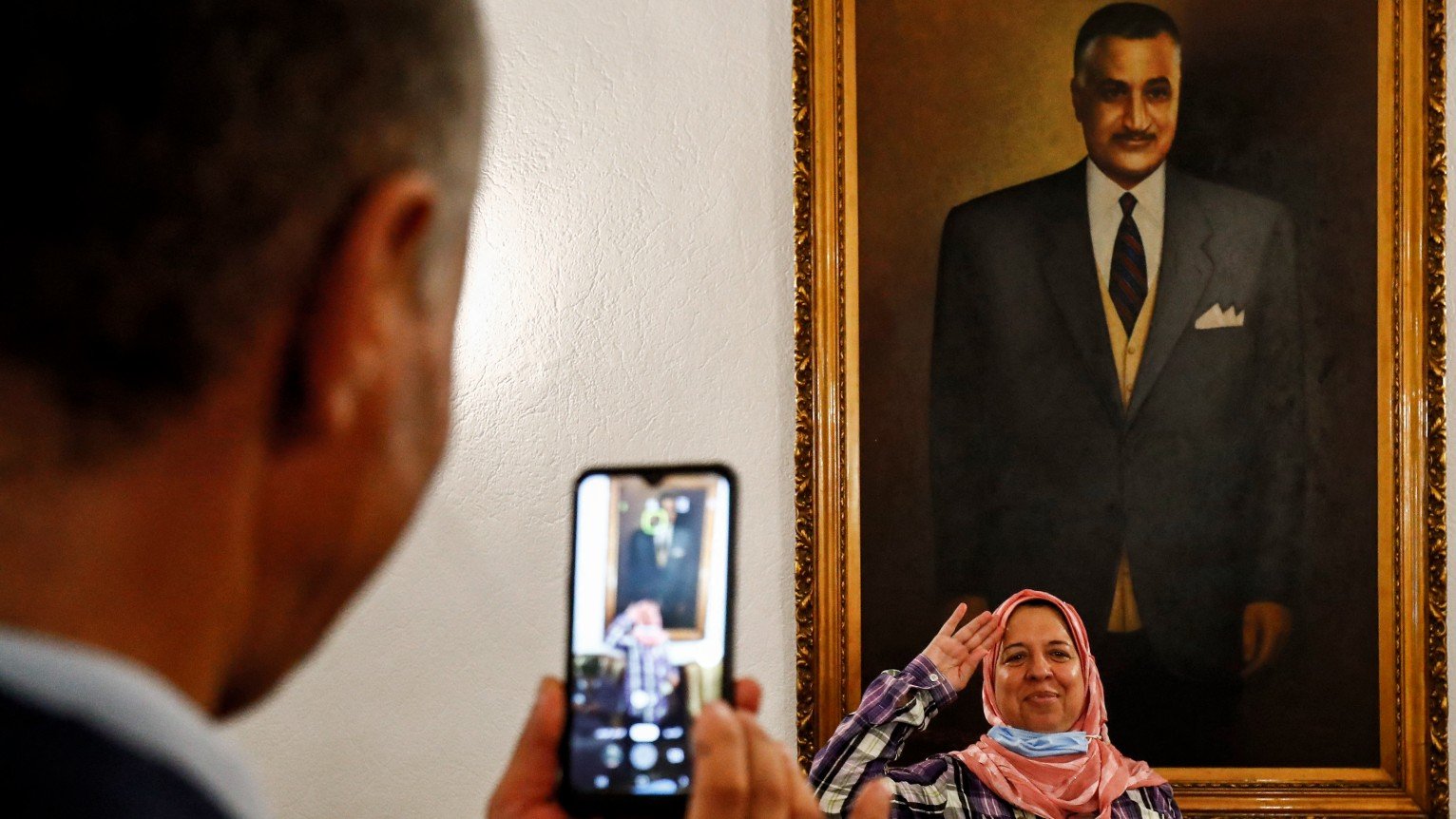A man uses his phone to photograph a woman giving a salute as she poses before a painting depicting Egypt's late president Gamal Abdel Nasser at his mausoleum in Cairo on 28 September, 2020 (AFP)