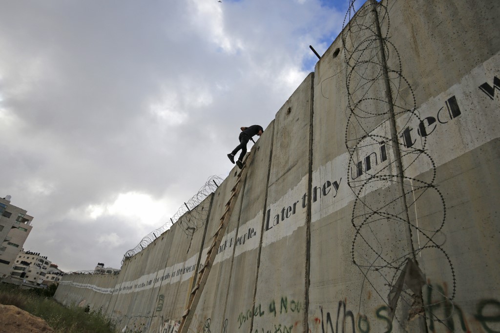A Palestinian youth climbs a section of Israel’s separation wall in Jerusalem on 10 May (AFP)