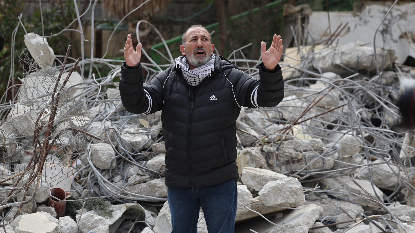 A Palestinian man reacts while standing on rubble after an Israeli military excavator demolished the house of Adham Bashir in the Jabal Mukaber neighbourhood of occupied East Jerusalem, on 13 February 2023 (AFP)