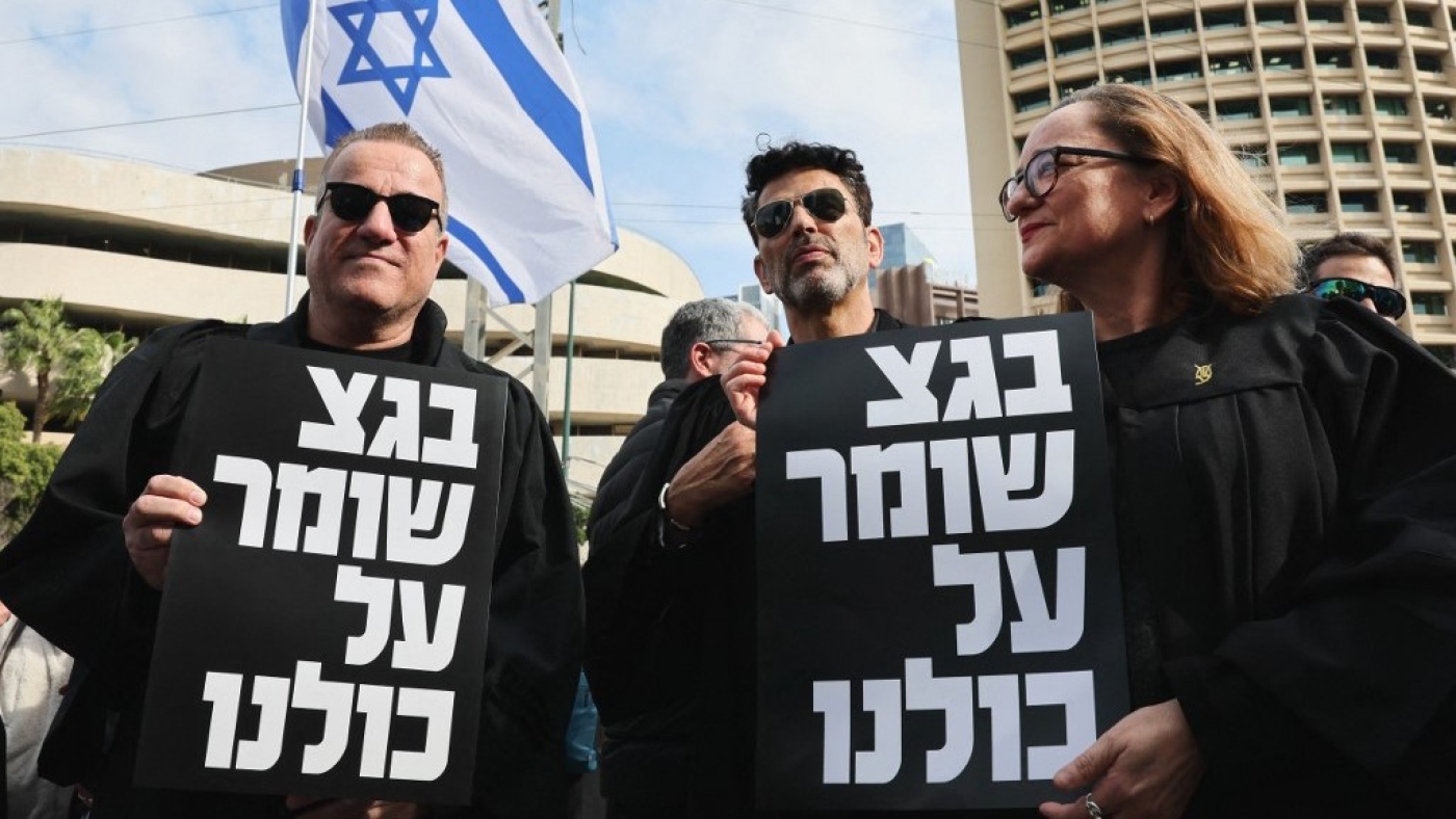 Lawyers hold signs with writing in Hebrew reading "the supreme court protects us all" during a demonstration by lawyers against the Israeli government's controversial plans to overhaul the judicial system, outside the Tel Aviv District Court of Justice on 12 January 2023 (AFP)