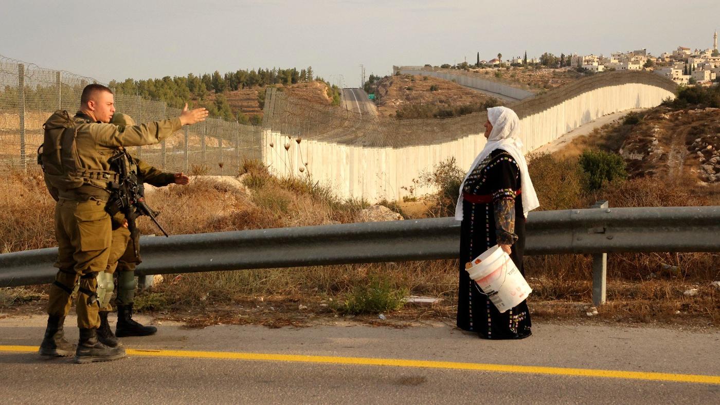A Palestinian woman stands near an Israeli army checkpoin on 13 October 2021 near Bait A'wa village on the outskirts of the occupied West Bank city of Hebron (AFP)