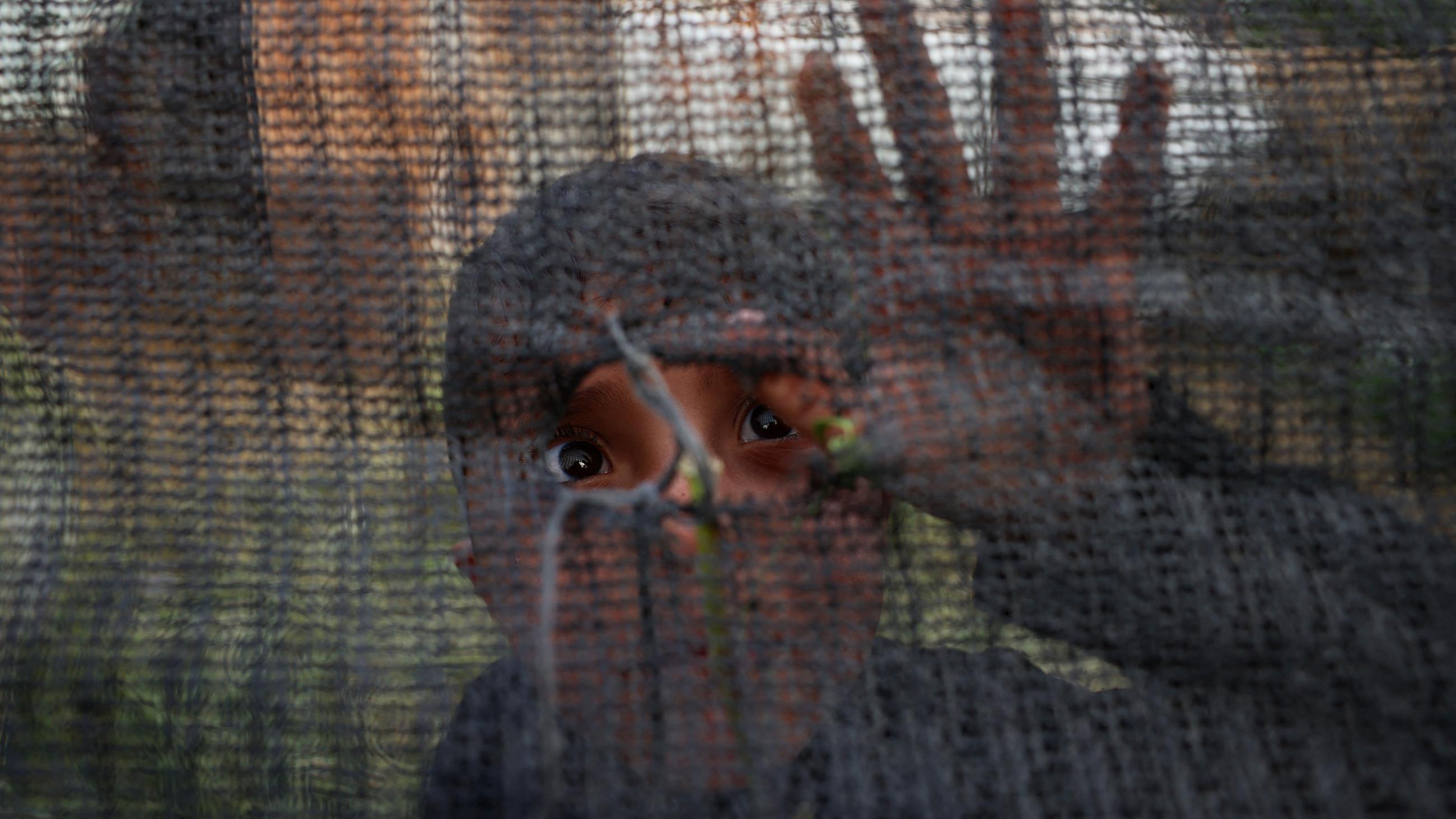 A Palestinian boy peeks out from a hole in a fence near al-Bureij in the Gaza Strip on 7 April 2022 (AFP)