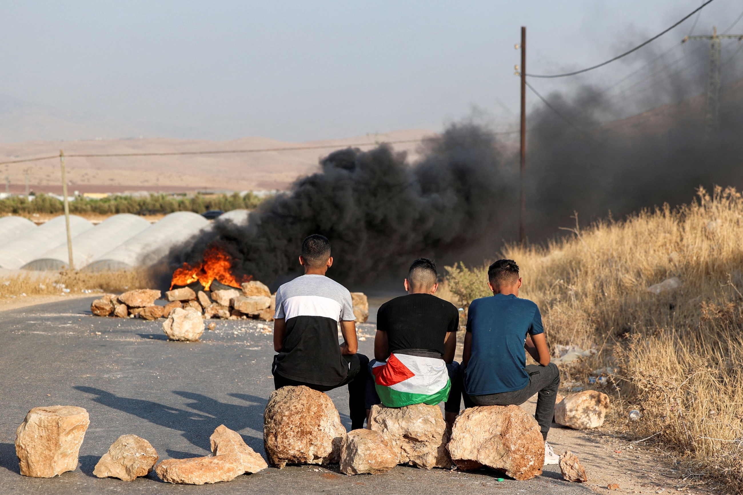 Palestinian men sit on rocks forming a make-shift barricade near flaming tires as they protest against the closure of a road near the site of an attack on an Israeli bus east of the Palestinian city of Tubas in the north of the occupied West Bank on September 4, 2022 (AFP)