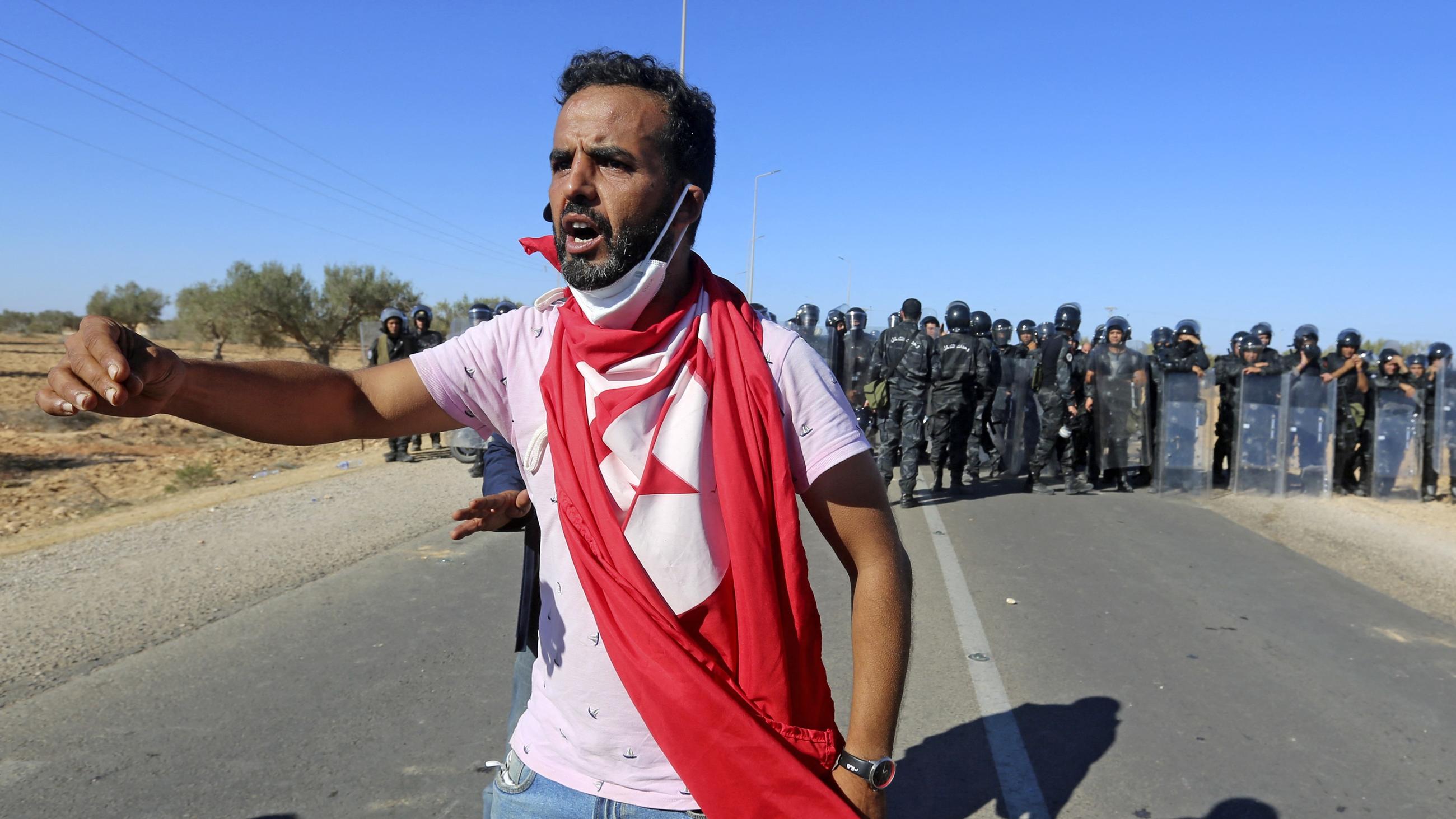 A man draped in a Tunisian national flag stands before security forces at a demonstration demanding an inquiry to determine the fate of migrants in Zarzis on 18 November 2022 (AFP)