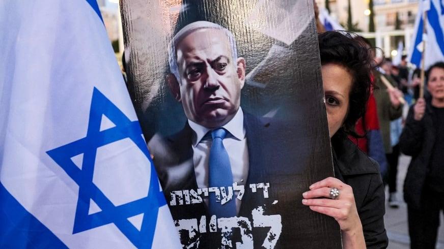 A demonstrator with a sign against Israeli Prime Minister Benjamin Netanyahu during a march against the government's judicial reform bill in Tel Aviv, 1 April 2023 (AFP)