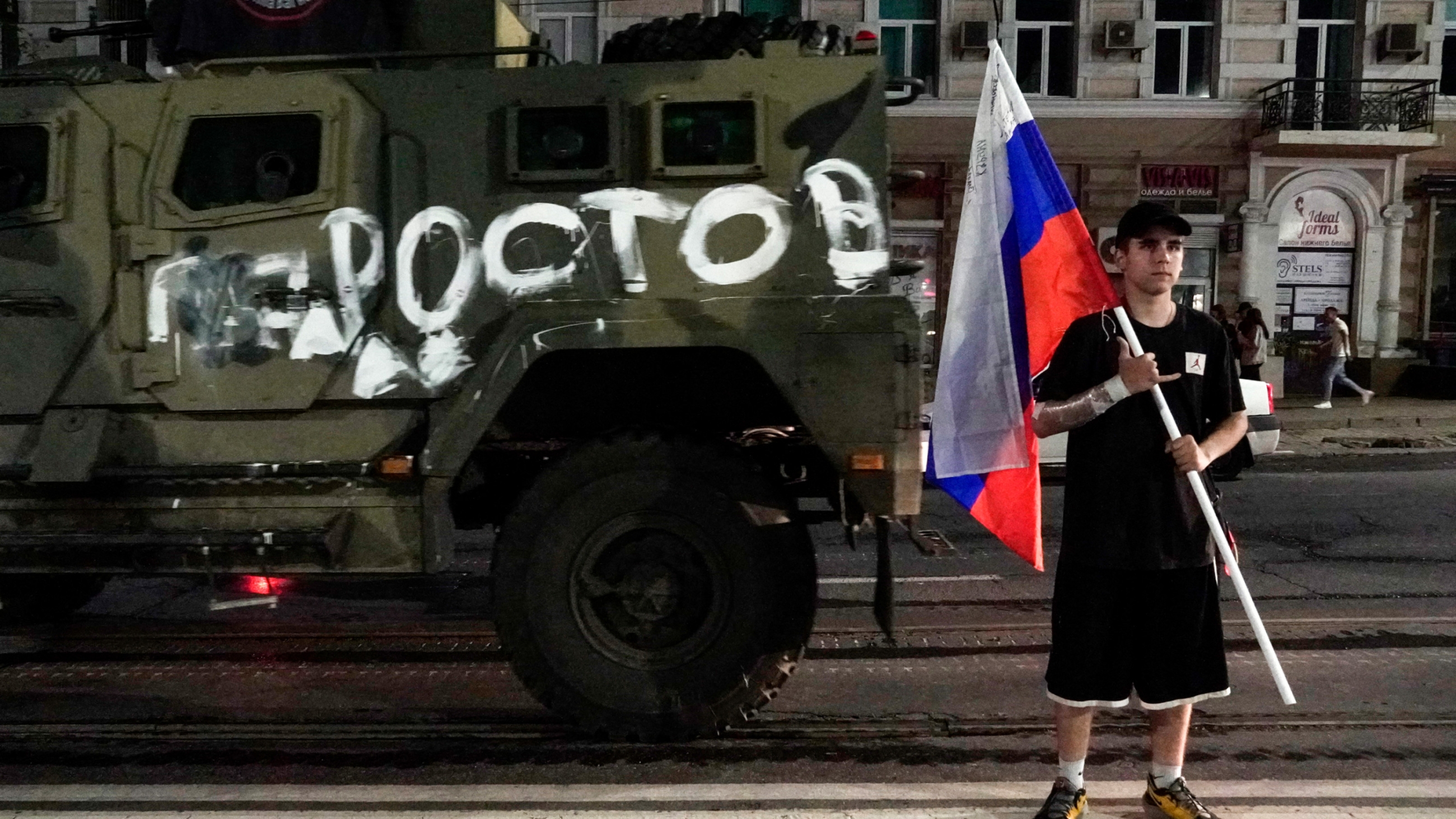 A man holds the Russian national flag in front of a Wagner group military vehicle with the sign read as Rostov, 24 June 2023 (AFP)