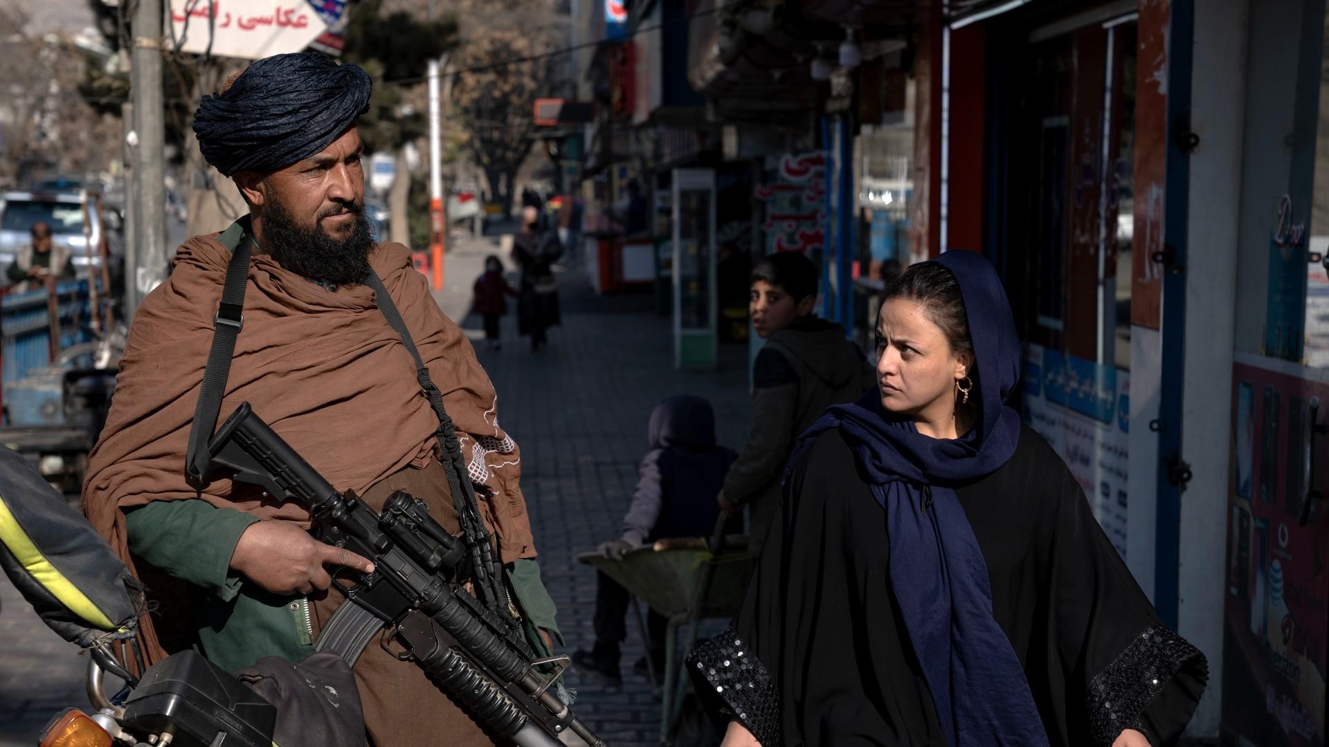 A Taliban fighter stands guard as a woman walks past in Kabul, Afghanistan, on 26 December (AP)