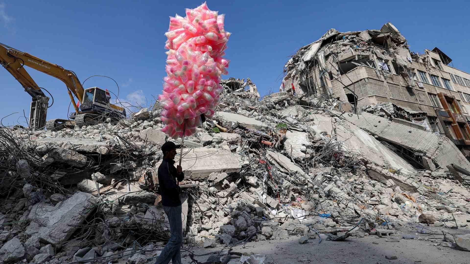 A Palestinian pedlar walks with bags of cotton candy past the rubble of a building destroyed during the May 2021 bombing of Gaza in Gaza City's al-Rimal neighbourhood, on 10 June 2021.