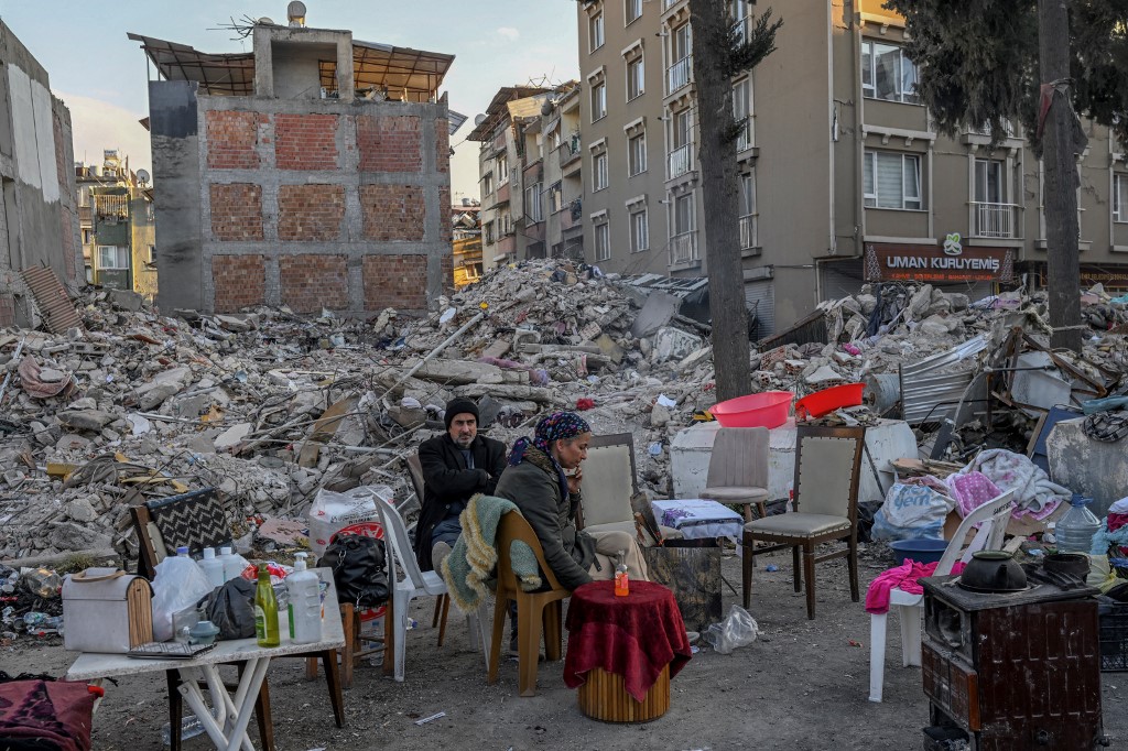People sit by collapsed buildings in Turkey’s Hatay province on 15 February 2023 (AFP)